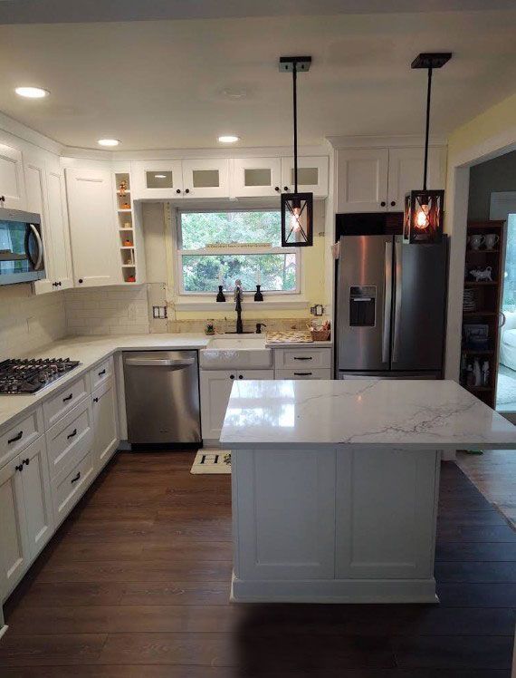 White kitchen with dark wood floors, stainless steel appliances, and an island.