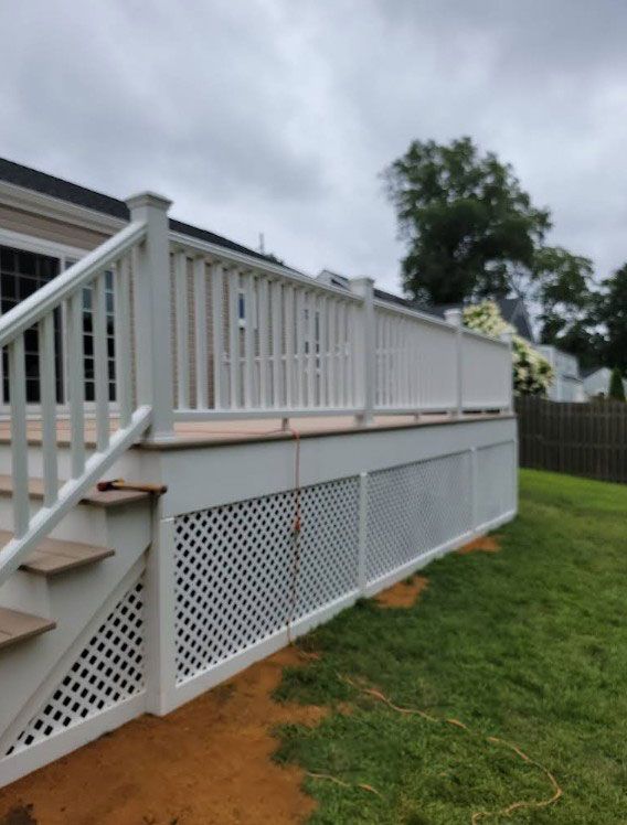 White deck with stairs, railing, and lattice skirting, next to green grass and a house.