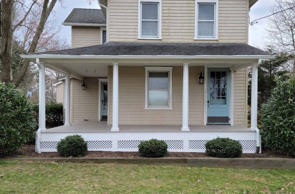Tan house with porch, white columns, blue door, bushes, and green lawn.