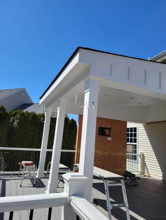 White-columned deck with roof, under construction, with a gray deck floor.