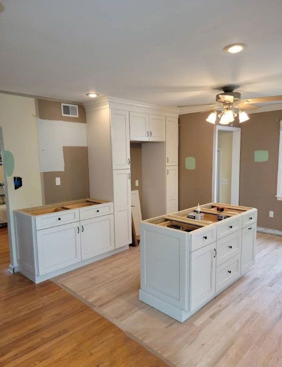 Kitchen under construction with white cabinets and two islands, wood floors, beige walls.