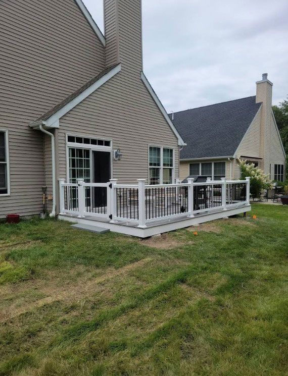 Deck with white and black railing attached to a beige house with green grass.
