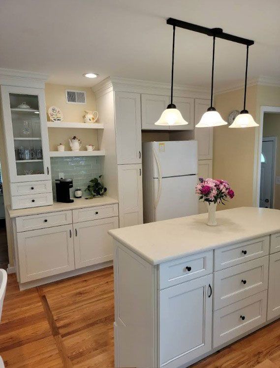 White kitchen with island, cabinets, and pendant lights; wood floors and refrigerator.