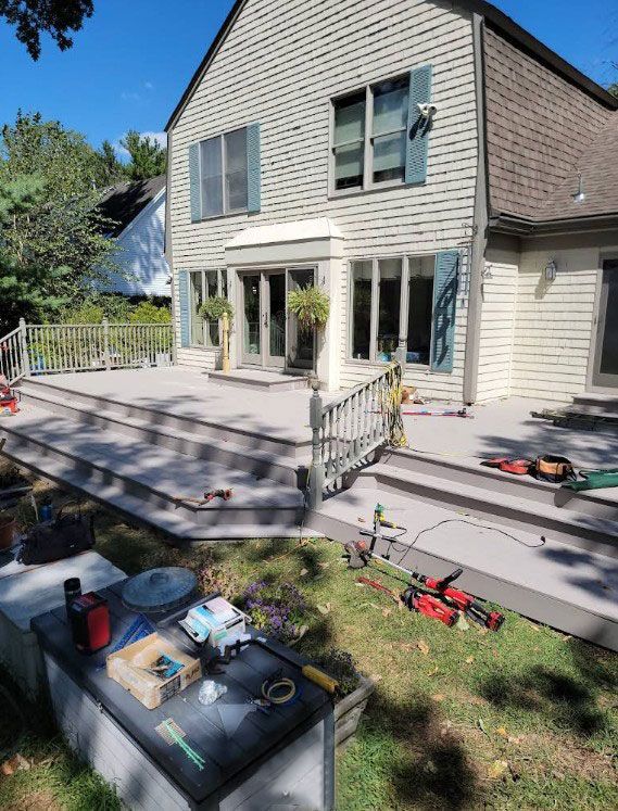 Backyard deck under construction, gray composite material, with tools visible. Light blue shutters on house.