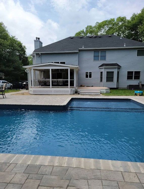 A backyard with a pool, patio, and screened porch on a two-story house.
