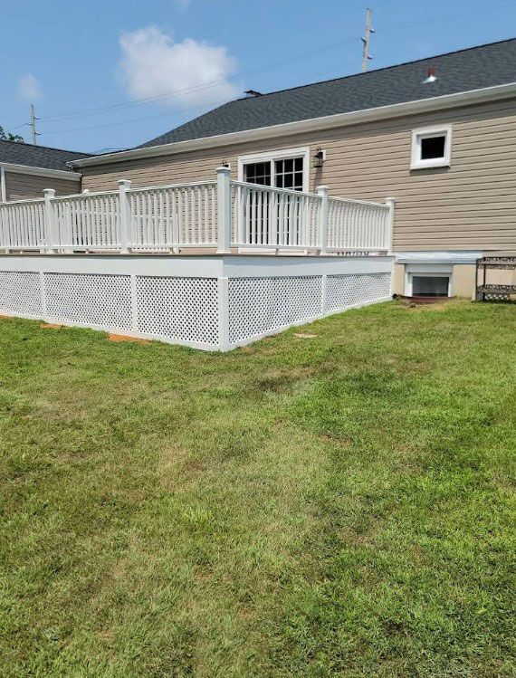 White deck with lattice skirting against a beige house with a sliding glass door, set on a grassy lawn.