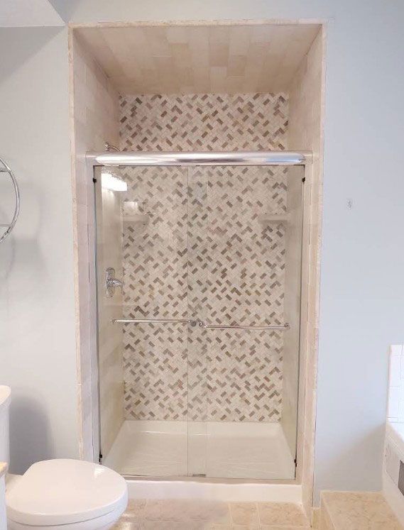Shower with glass doors and a patterned tile backsplash in a recessed alcove.