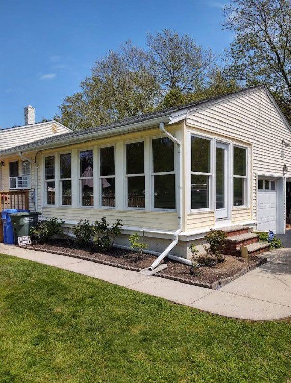 Yellow house with sunroom, garage, and front lawn. 