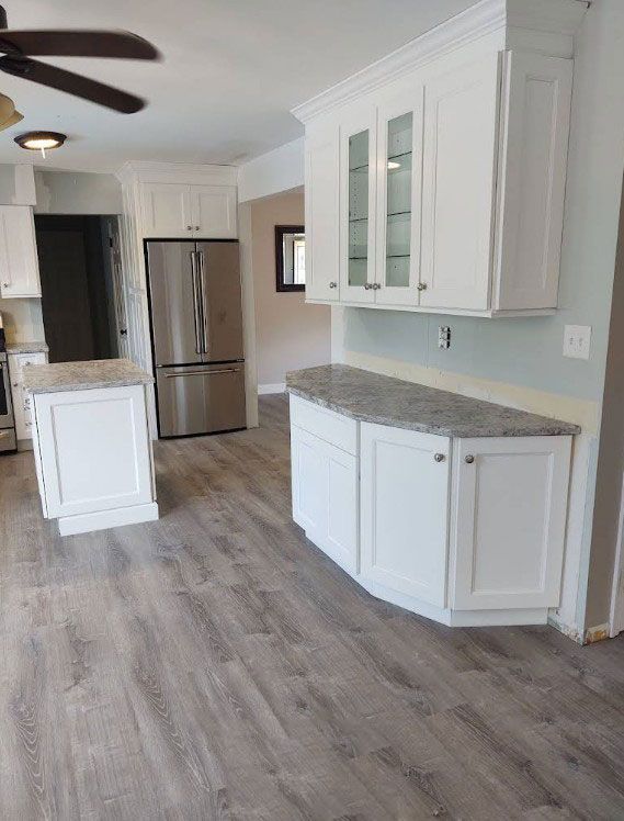 Modern white kitchen with granite countertops, stainless steel appliances, and wood-look flooring.