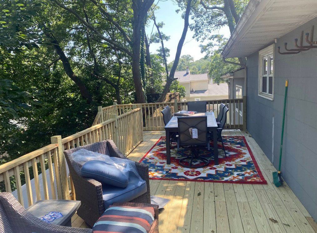 Wooden deck with furniture, table set, rug, and blue accent pillows.