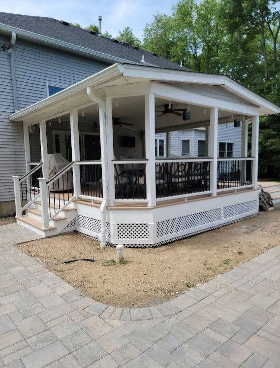 Screened-in porch attached to a house. White trim, gray deck, black railings. Outdoor seating.