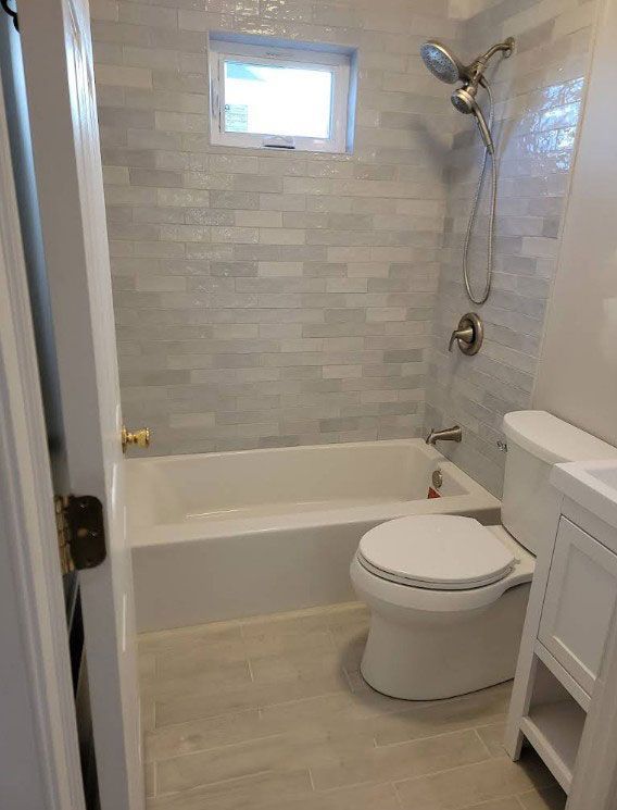 Small, newly renovated bathroom with white fixtures, gray tile, and a small window.