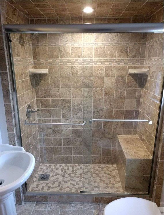 A tiled shower with a built-in bench, glass doors, and a small sink.