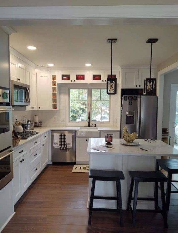 White kitchen with stainless steel appliances, island with stools, and pendant lights.