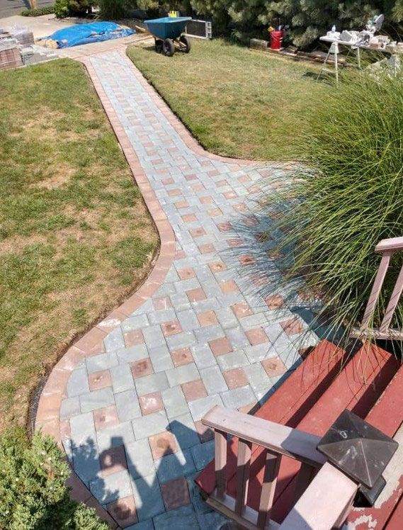 Brick walkway with red and blue pavers, leads from steps through a grassy yard.