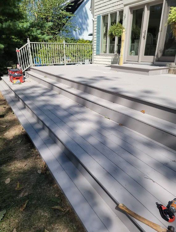 Gray deck with steps leading up to a house, with green grass and a white railing.