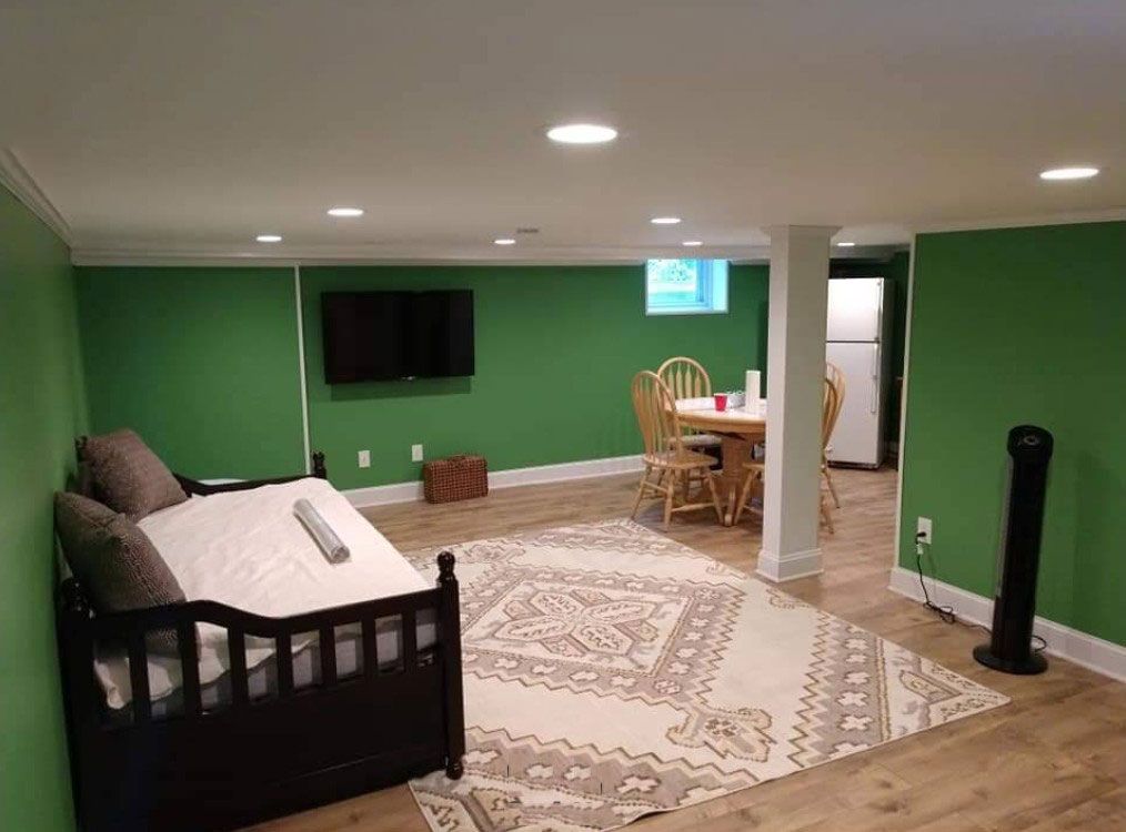 A green-walled basement room with a sofa, TV, table, rug, and fan.