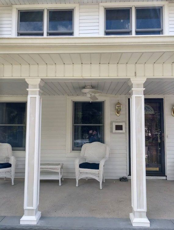 White house porch with columns, wicker furniture, and front door.