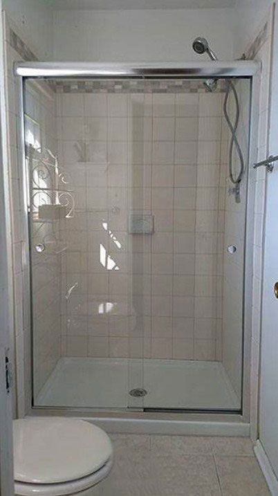 Shower stall with sliding glass door, white tiles, and a toilet in a bathroom.