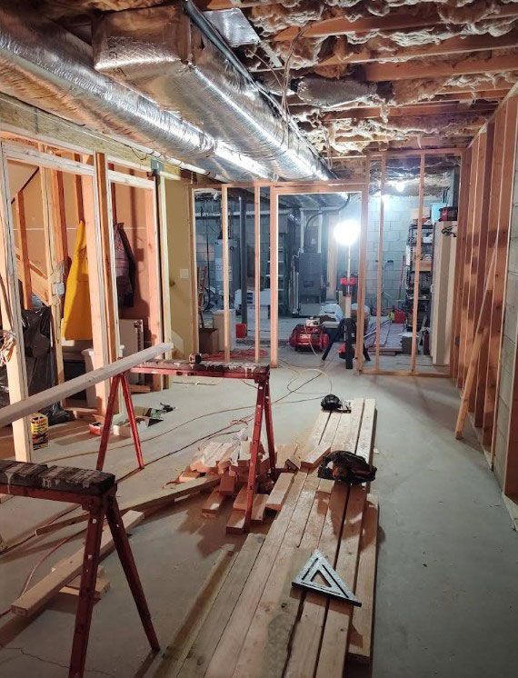 Basement renovation in progress: wood frames, tools, exposed ceiling. Interior construction scene.