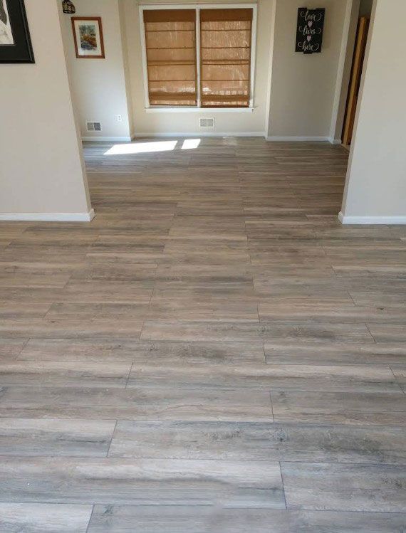 Light-colored, wood-look tile flooring in a room with a window and beige walls.