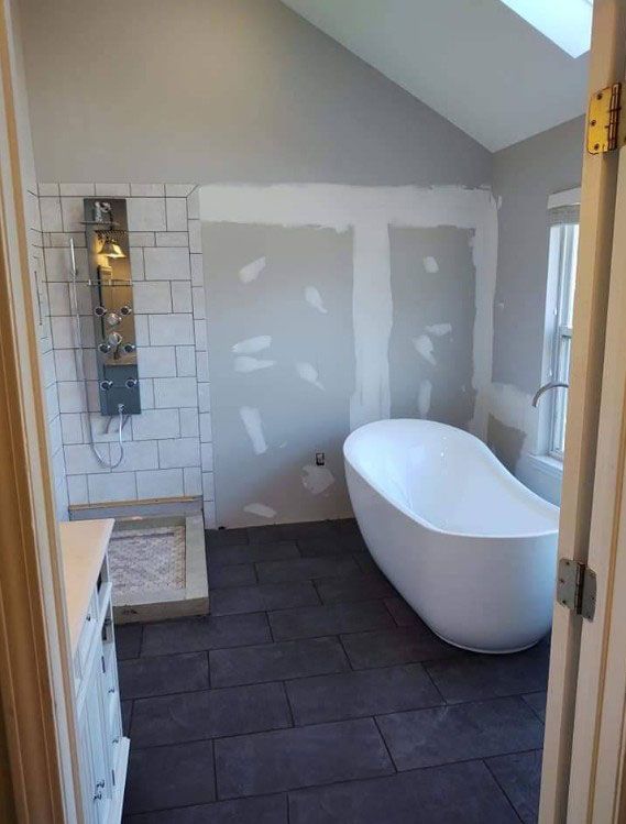 Bathroom under construction with a freestanding tub and a tiled shower. Gray walls and dark tile floor.