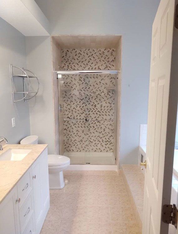 Bathroom with light blue walls, white vanity, and patterned tile shower.