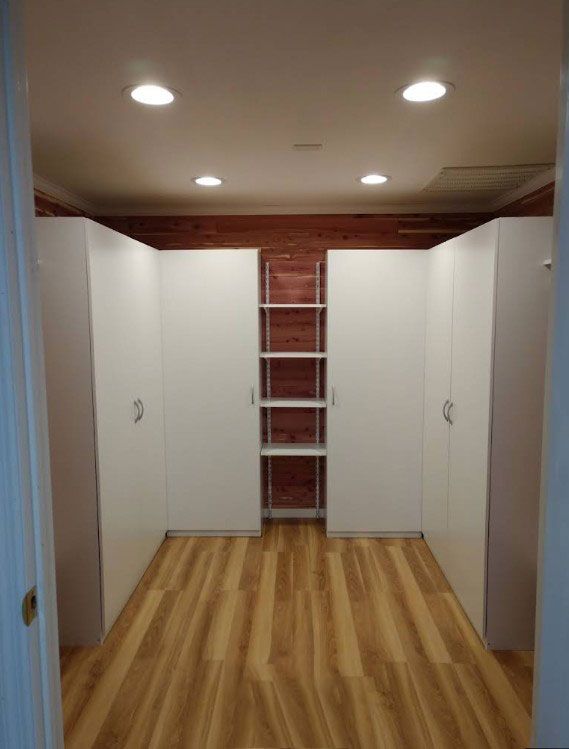 A modern walk-in closet with white cabinets, wooden floor, and recessed lighting.