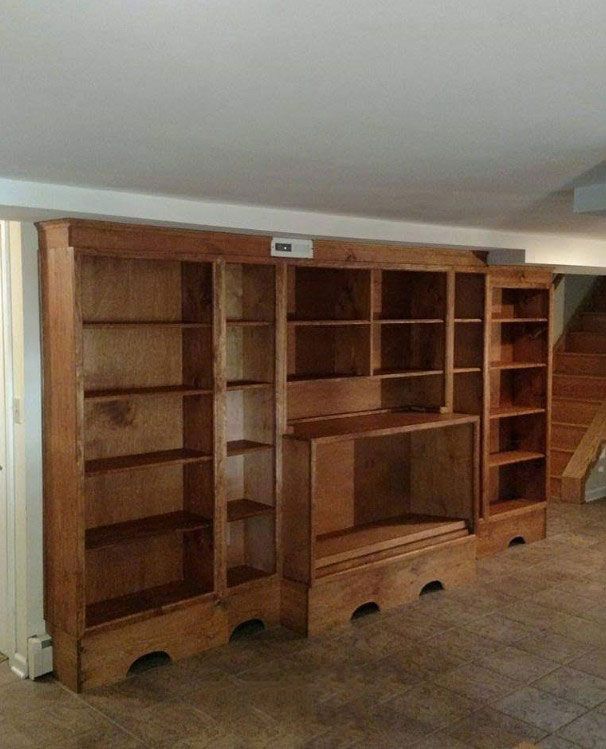 Large wooden built-in bookshelves with several shelves and a cabinet, in an unfinished room.