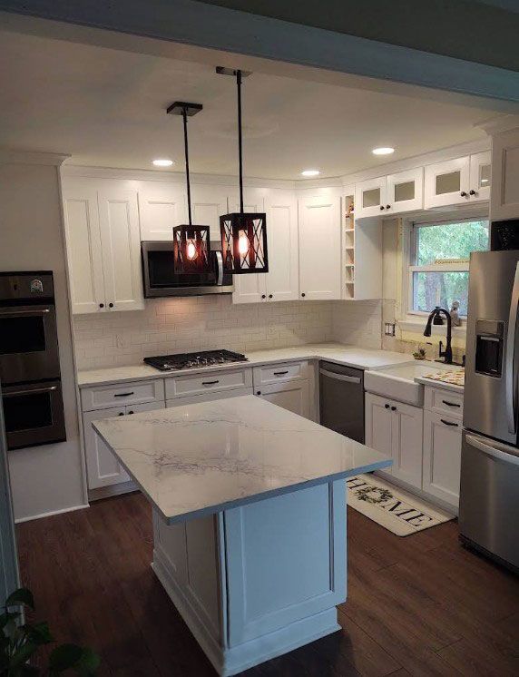 White kitchen remodel with island, pendant lights, stainless steel appliances, and dark wood floors.