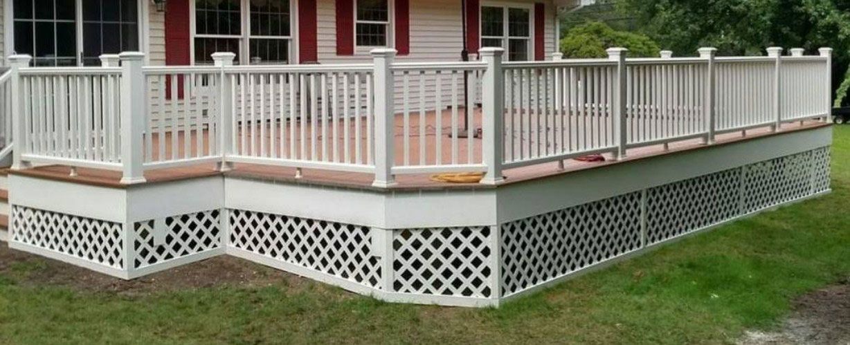 White deck with lattice skirting, railing, and a house in the background.
