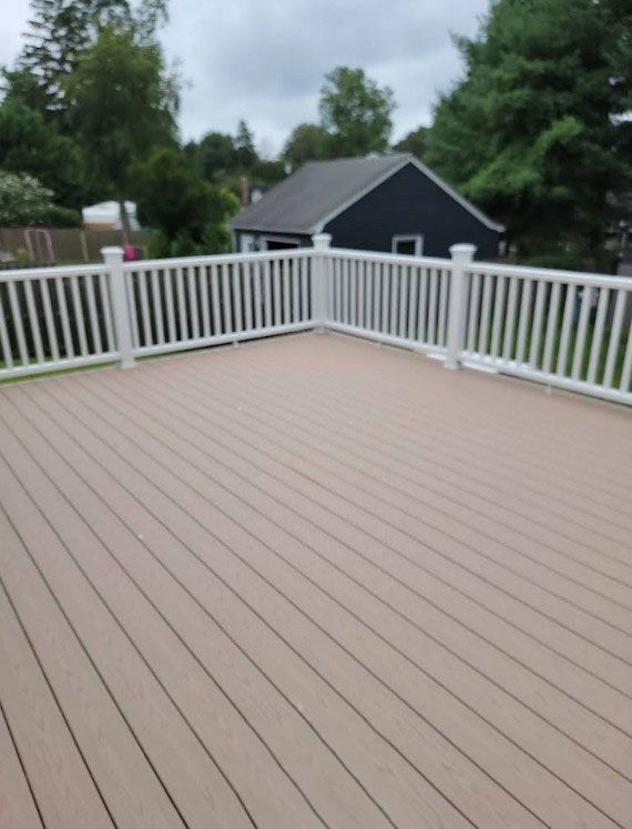 Wooden deck with white railing, dark blue shed in the background, overcast sky.