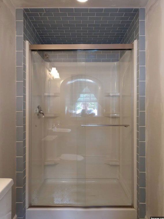 Shower stall with glass doors, surrounded by grey tile.