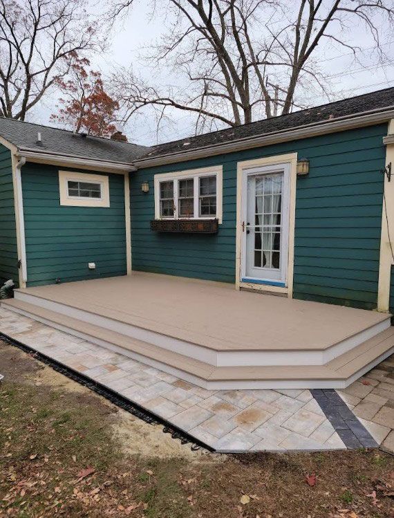 Green house with a new tan deck, stone path. Cloudy sky.