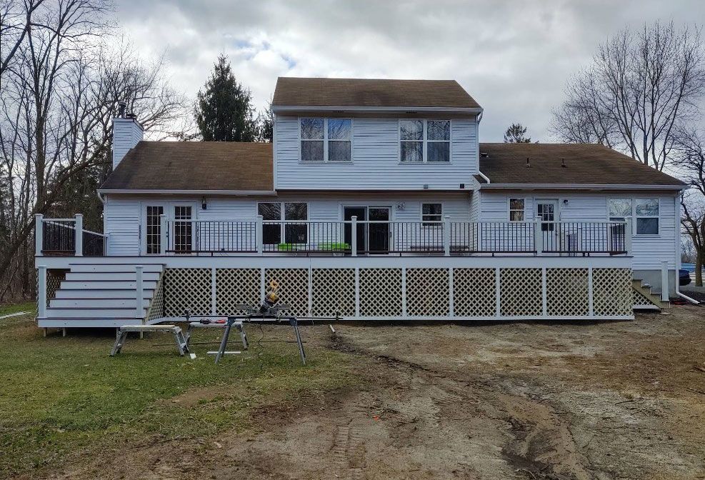 White two-story house with a large deck and latticework on a cloudy day, construction tools in view.