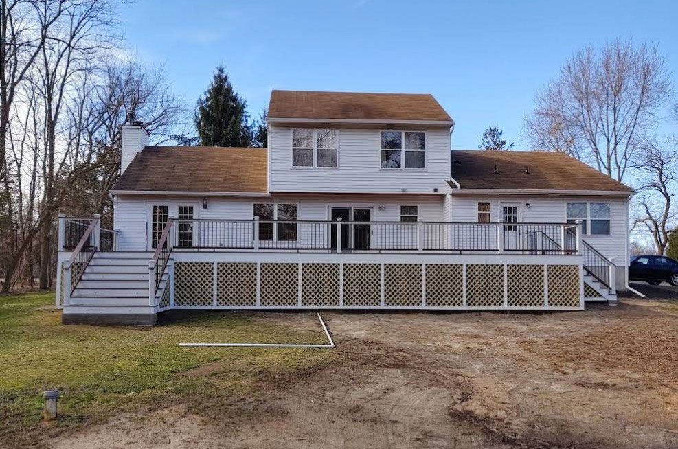 Two-story white house with brown roof and large deck, on a grassy lot.