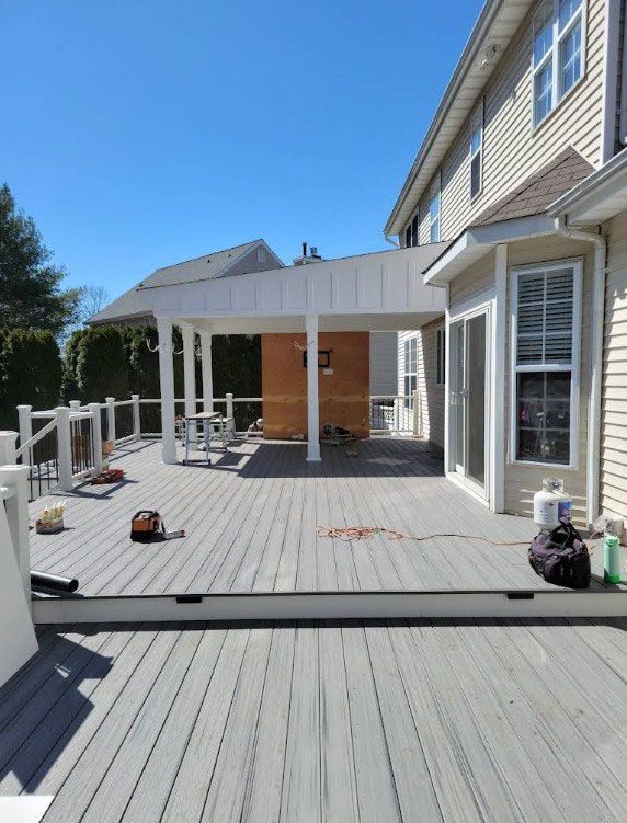 Grey composite deck with a white pergola and railing attached to a beige two-story house on a sunny day.