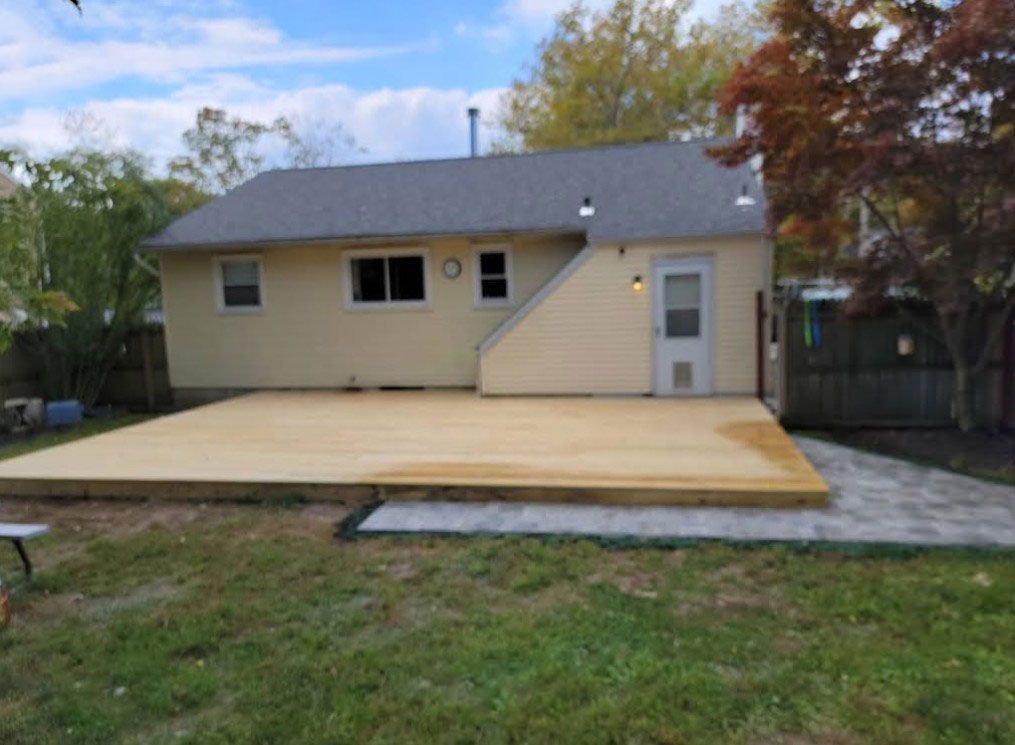 Backyard with a new wooden deck, concrete patio, and light yellow house; green grass, autumn trees.
