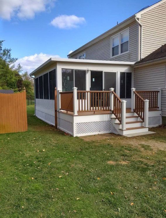 Screened porch attached to a two-story house with stairs, a wooden deck, and a white lattice base on a grassy lawn.