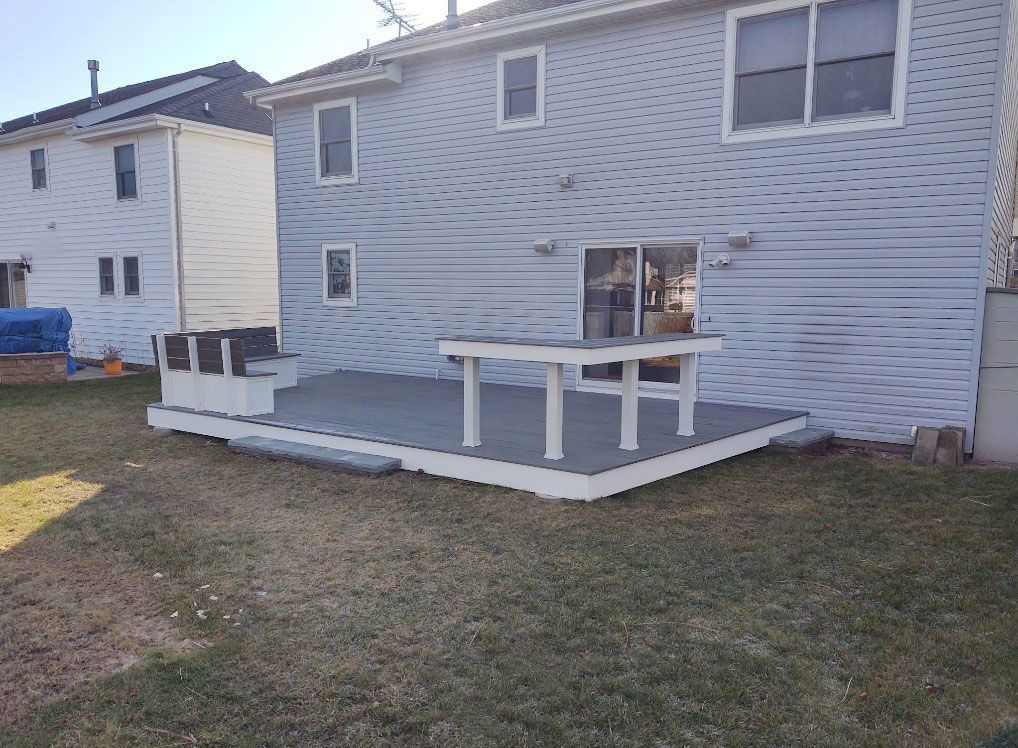 Backyard deck with grey flooring, white trim, and a matching table. House in background.