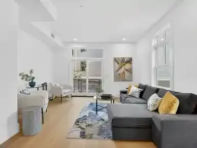 Bright modern living room with gray sectional, patterned rug, wall art, and large windows.