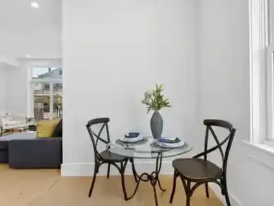Small dining table with two black chairs in a bright, minimalist room near large windows.