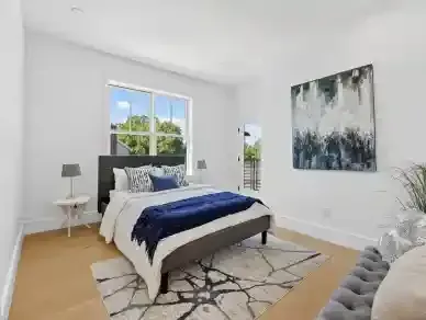 Bright bedroom with white walls, gray bed, navy blanket, patterned rug, and abstract wall art
