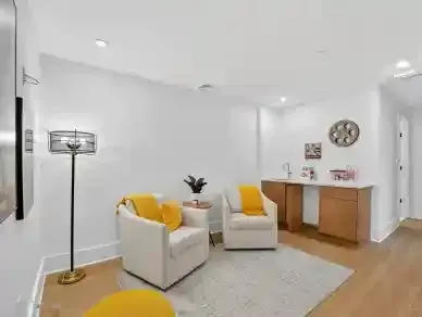 Bright white living room with two cream chairs, yellow pillows, a floor lamp, side table, and wooden console.