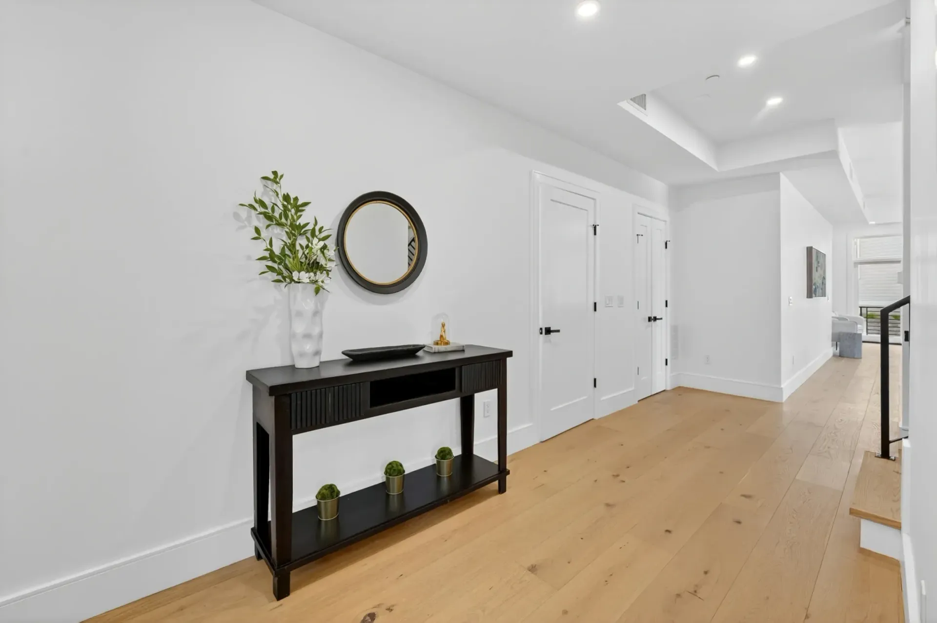 Bright hallway with black console table, mirror, potted plant, and white double doors on light wood floor