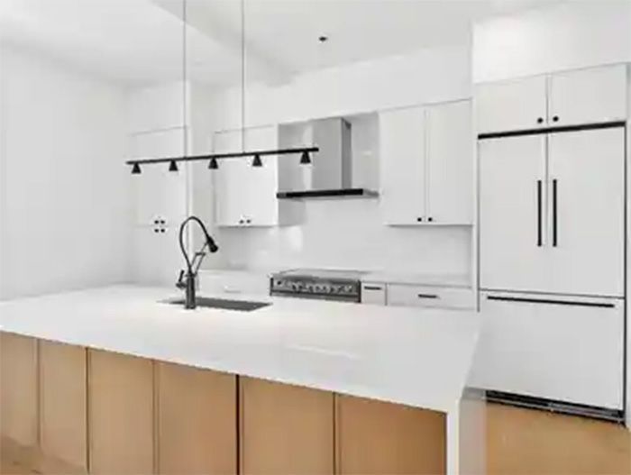 Modern white kitchen with wood-front island, black fixtures, and stainless steel refrigerator