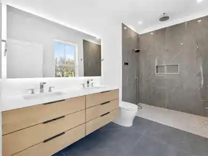Modern bathroom with double vanity, large mirror, gray shower, and blue floor tile.