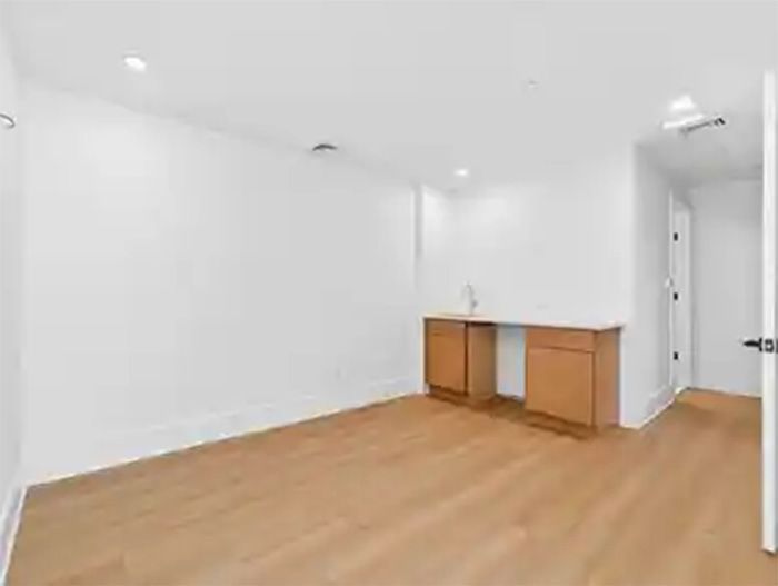 Empty white room with wood floor, small cabinet, and an open doorway