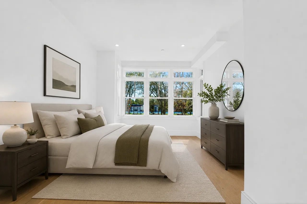 Bright bedroom with a neatly made bed, large windows, and modern dark wood accents