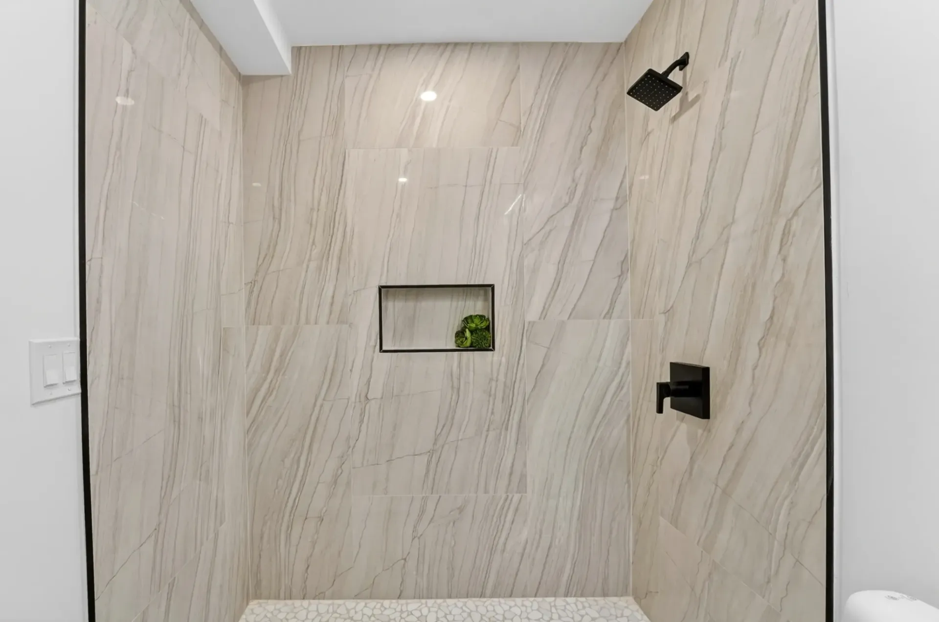 Modern bathroom shower wall with light stone tile, recessed niche, and black fixtures